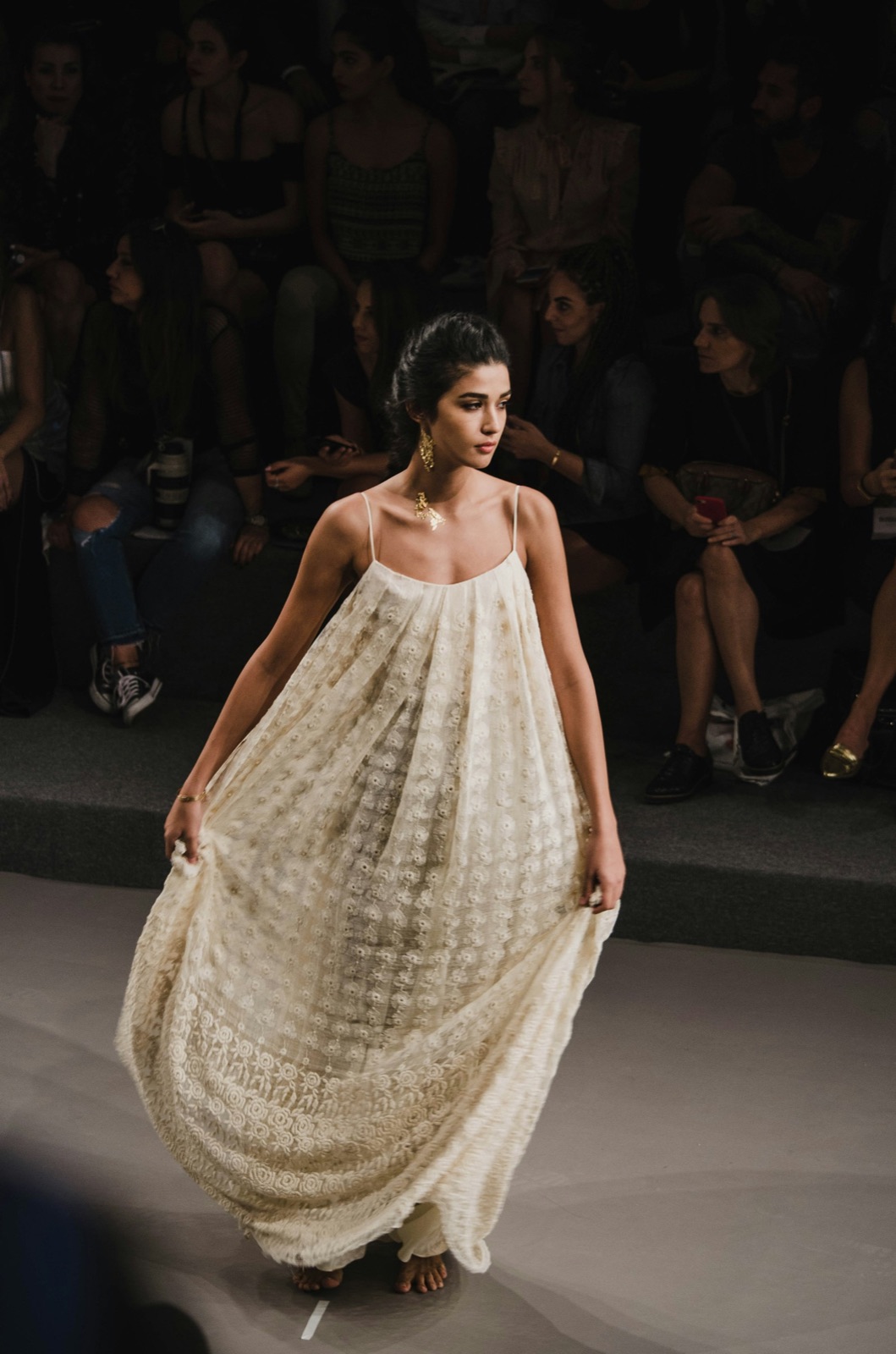 Người mẫu trình diễn đầm hai dây xếp ly màu kem trên sàn runway