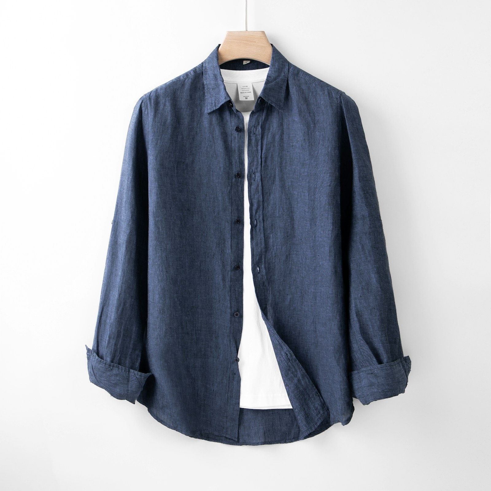 Sơ mi linen màu xanh chàm treo trên móc gỗ, nền tường trắng