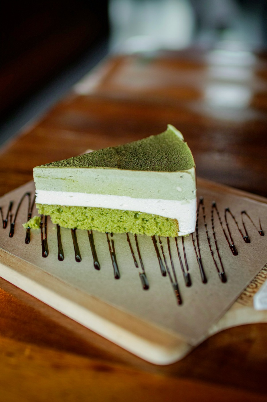 Lát bánh basque matcha nhiều tầng với sốt chocolate kẻ trên khay