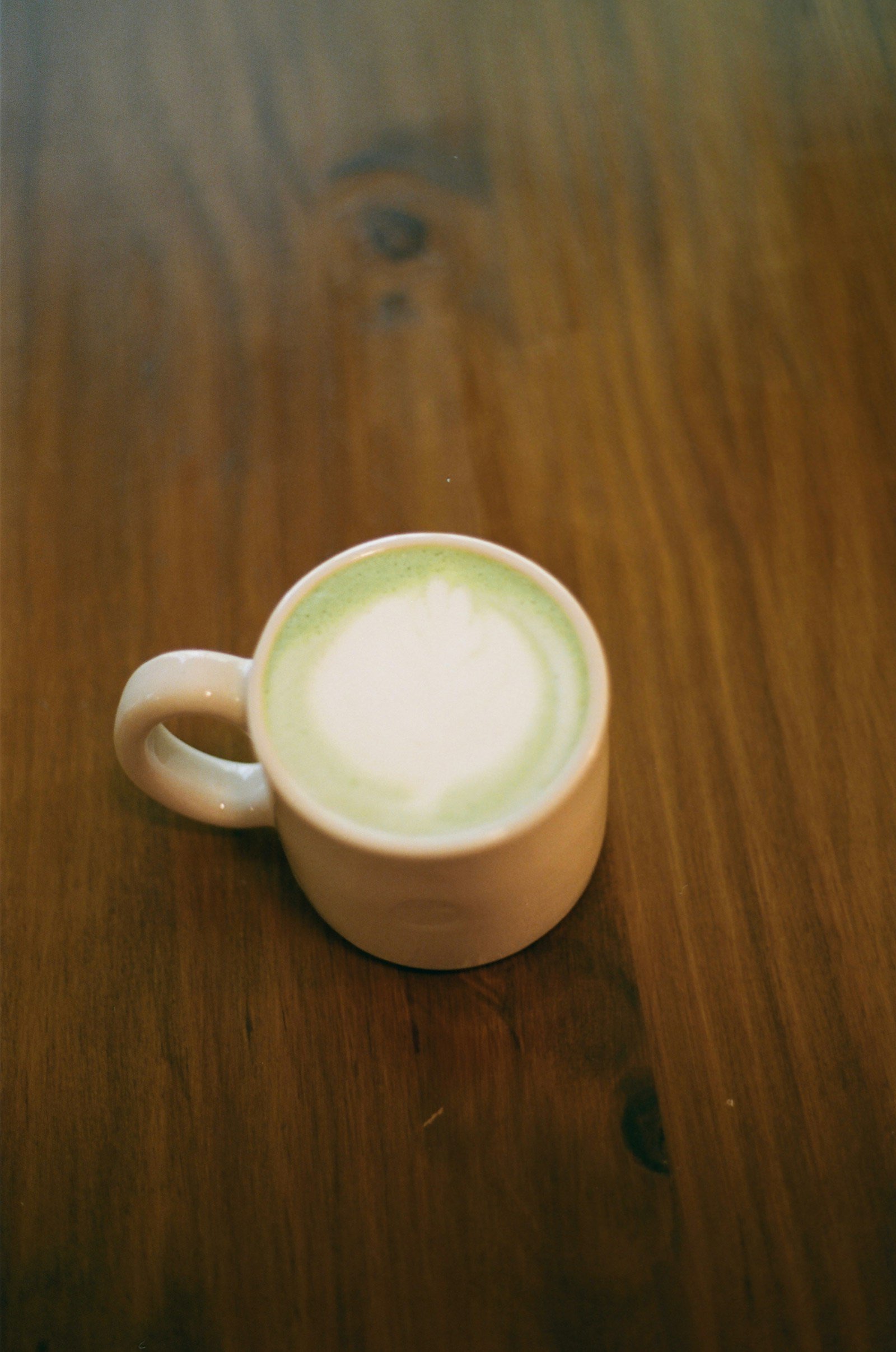 Matcha latte nóng trong cốc sứ trắng trên bàn gỗ